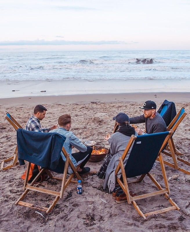 four-people-gathered-around-a-fire-pit-on-a-beach-near-the-ocean-portsmouth-nh